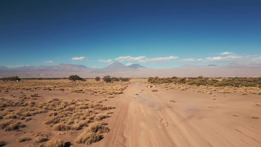Aerial of a car traveling down a dirt road in a vast sunny desert