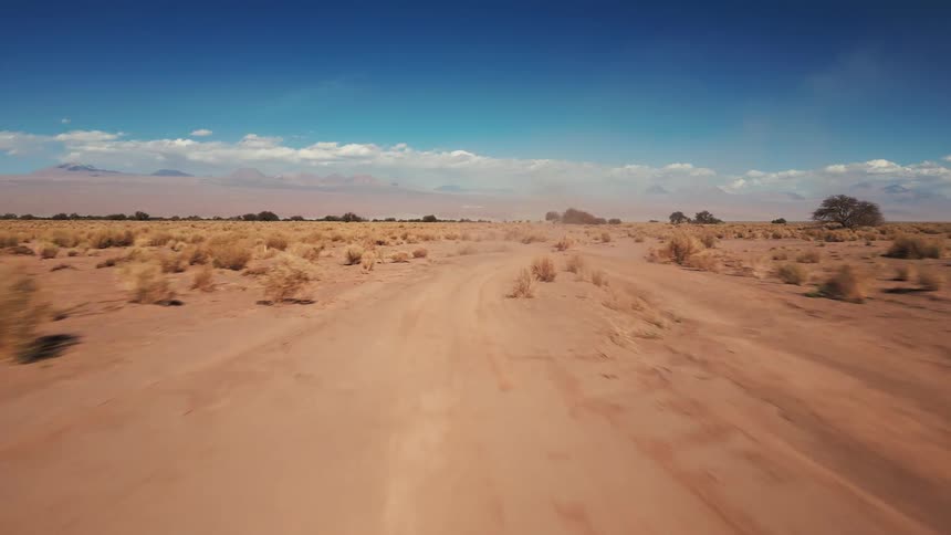 A fly over shot of the desert as a jeep drives down a dirt road