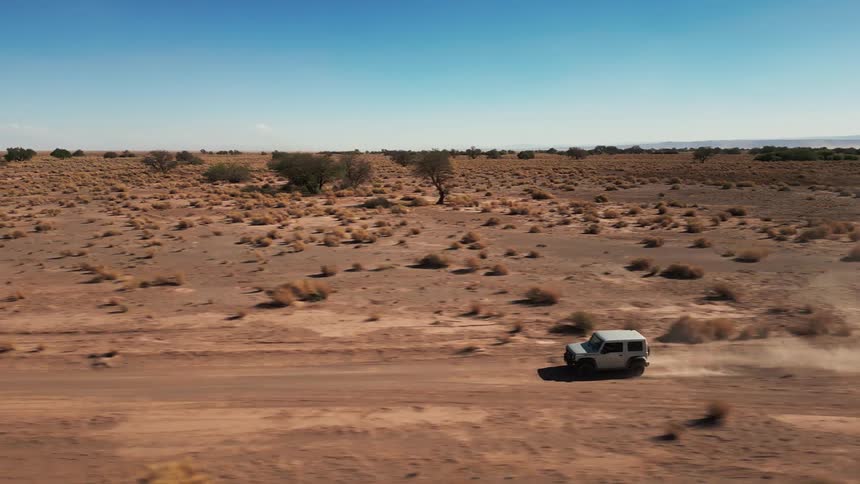 A white jeep drives across a desert