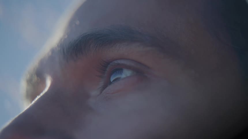 A closeup of a persons eyes reflects the blue sky and clouds