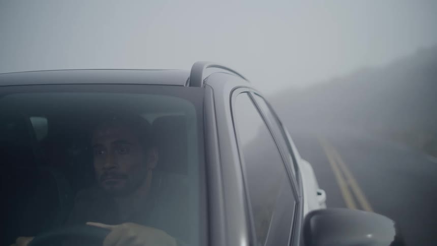 A man driving a black car on a fogcovered road
