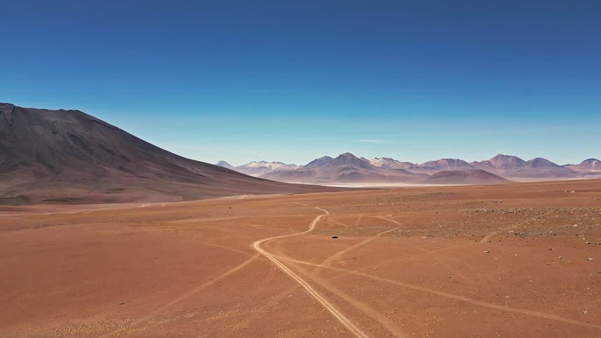 Motorcycle tracks in the desert near a dune in front of the mountains