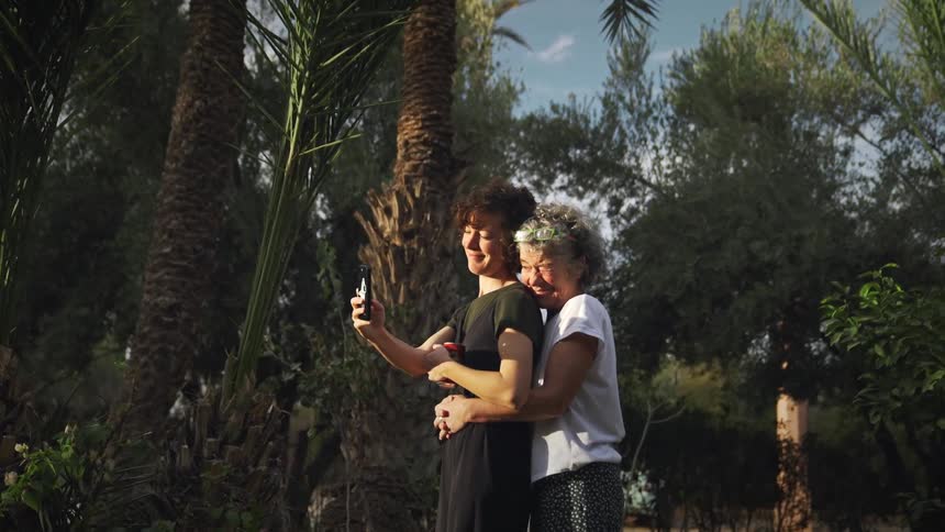 Two women hug while using a smartphone