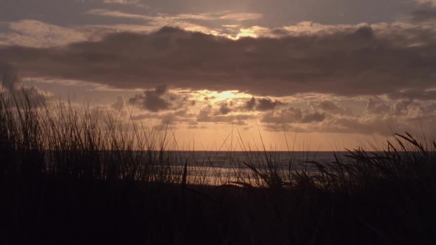 The sun is obscured by a layer of clouds above a coastal beach