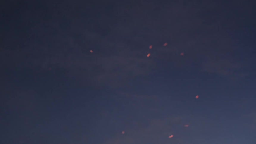 A piece of wood burns against a twilight sky with sparks and flames visible