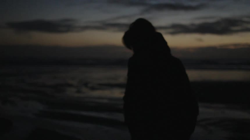 A silhouette of a person walking on a beach on a dark morning
