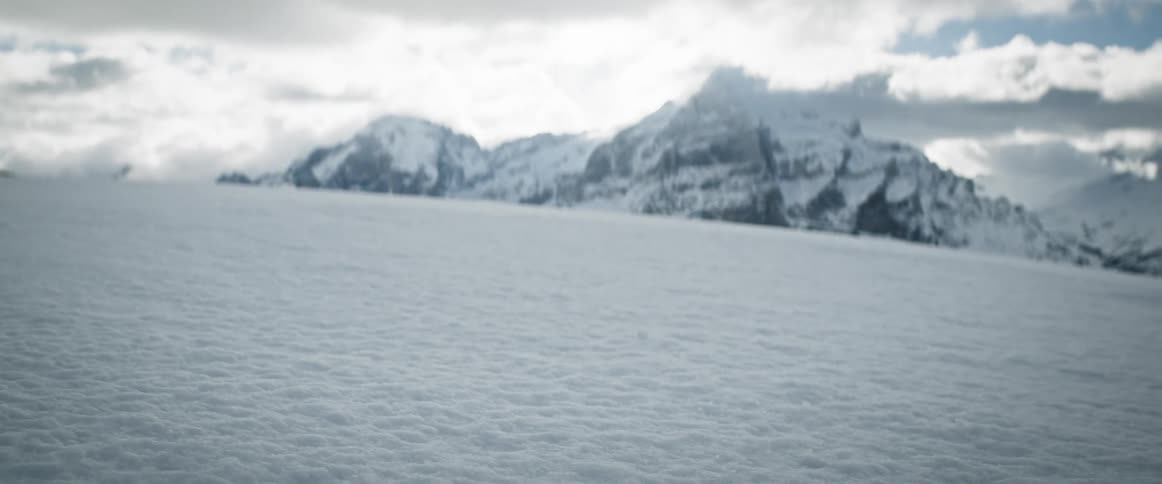 A vast snowy landscape with majestic mountains in the background under a cloudy sky