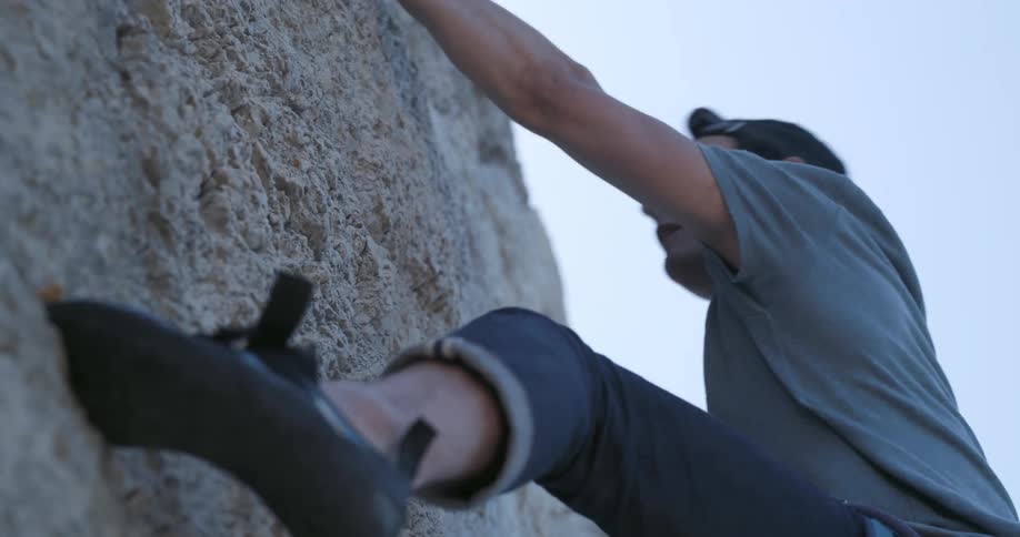 Concentrated man climbing a rock wall in a risky way during the day