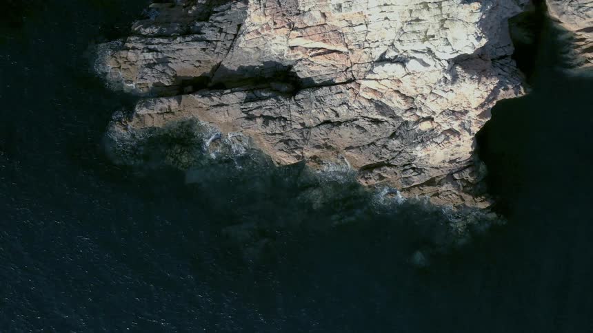 Top down aerial view of ocean waves crashing on a rocky coast