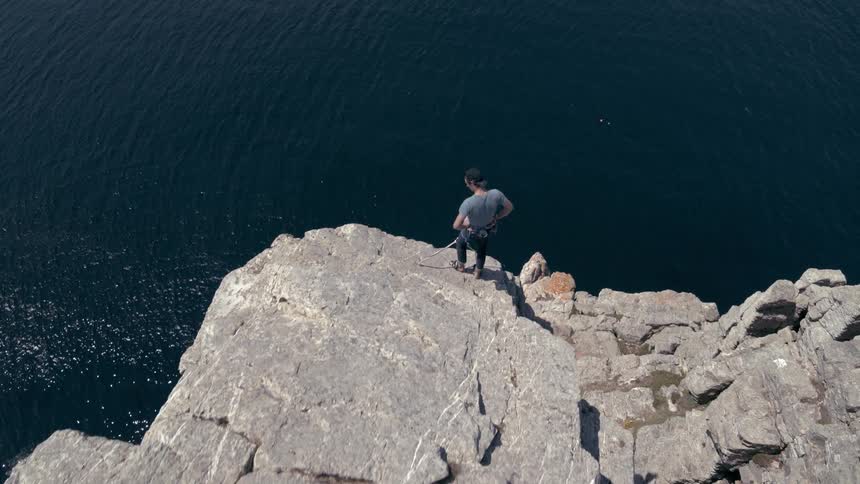 A rock climber looks down after reaching the top of a cliff over the ocean
