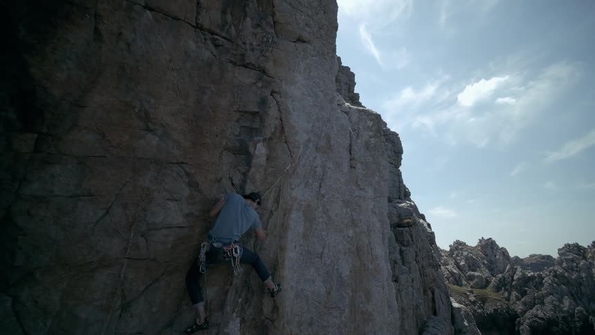 A man is climbing a rocky mountain under a clear sky