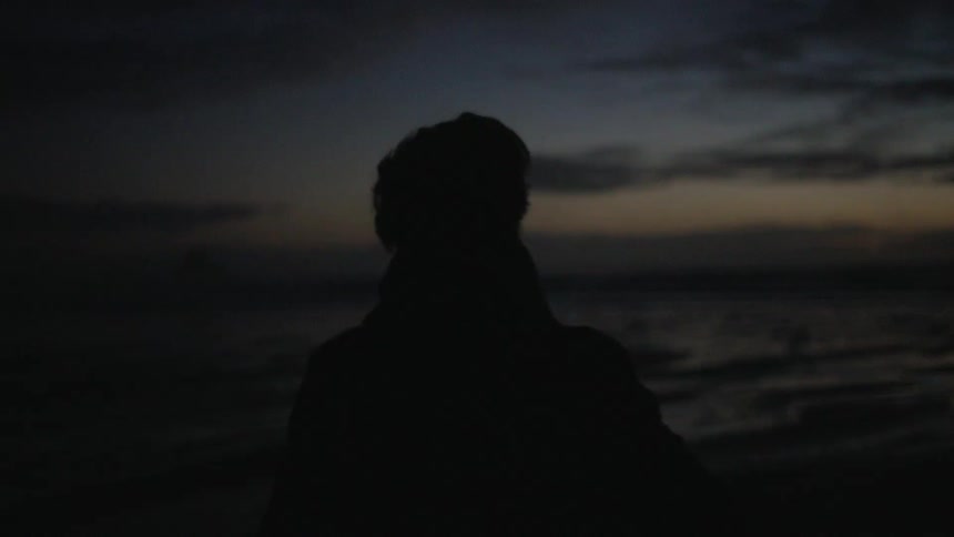 Silhouette of a person walking in a natural environment with water around them on a dark sky morning