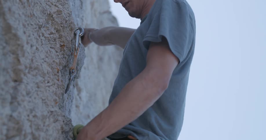 Man climbing a rock wall of a mountain and placing protective belts in the rock