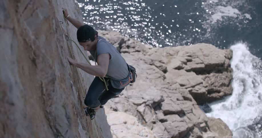 A rock climber carefully ascends a rocky cliff above the ocean