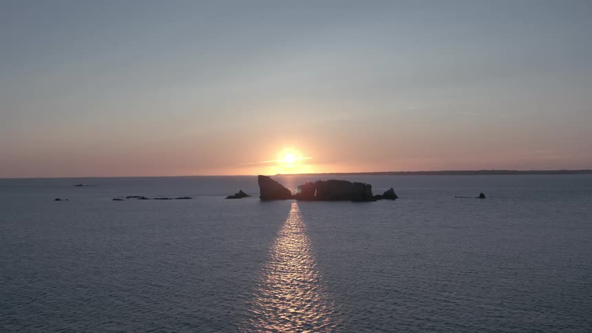 Landscape of rocks in the middle of the ocean with a sun on the horizon