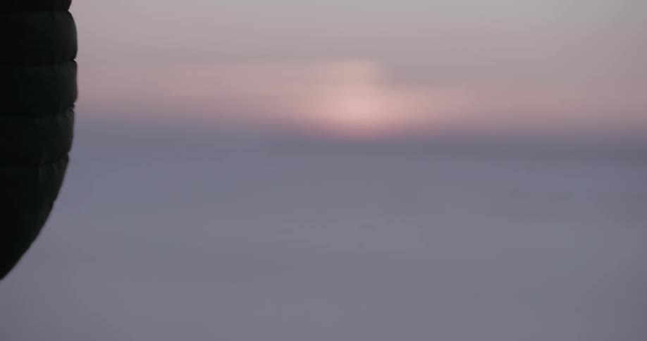 Arm of a man collecting a rope while standing outdoors with the blurred and reddish morning sky