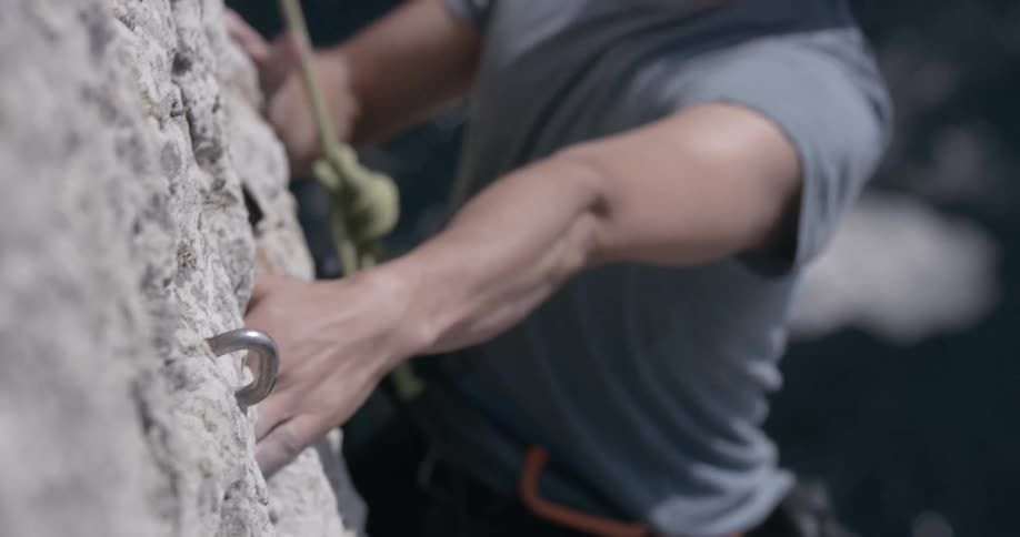 Closeup on the hands of a man who is climbing a mountain wall in abyss to the sea