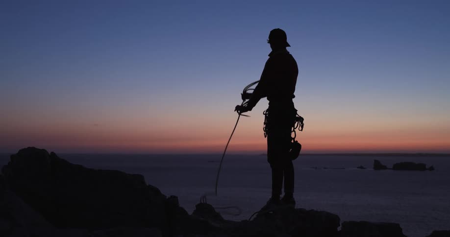 A male wrapping rope around outdoors at dusk on a rocky mountain