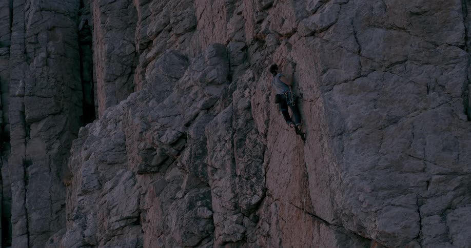 A lone climber scaling a steep rock wall with no visible safety equipment