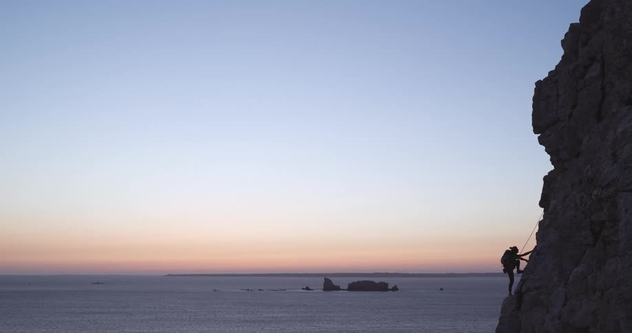 Woman climbing the rocky coast next to the sea on a red sky morning
