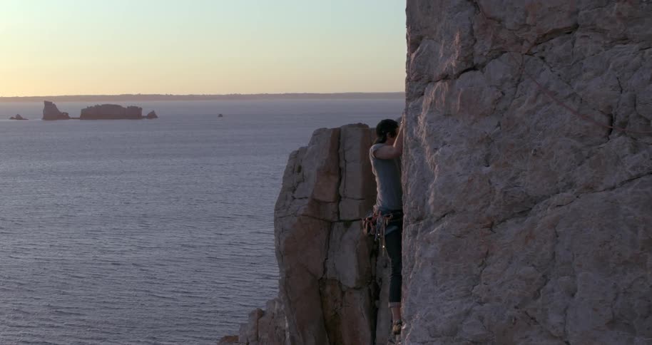 A climber climbing a cliff during sunset with the sea in the background