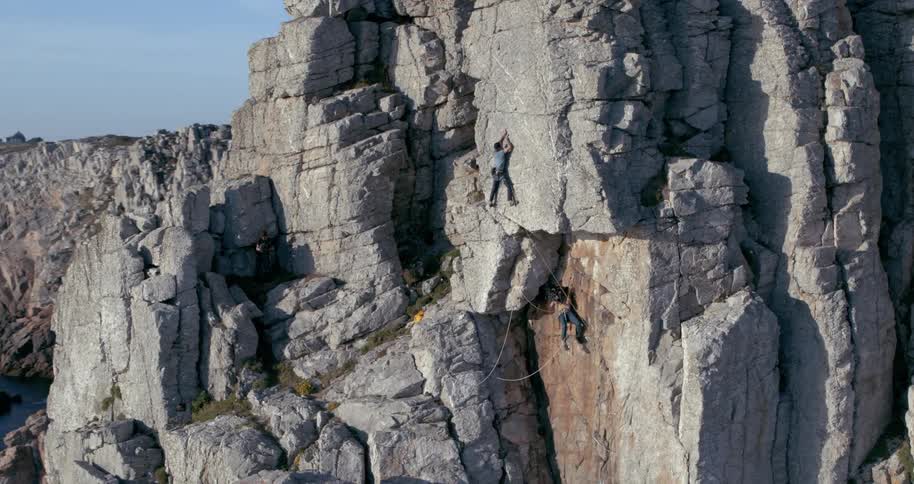 Two people are rock climbing on a rugged cliff beside the ocean