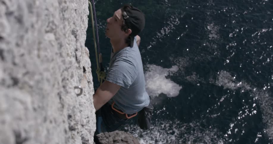 Adventurous man passing magnesium on his hands while concentrating and taking risks hanging from a rocky mountain wall in freefall to the sea