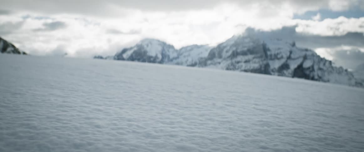 A flat ground covered in snow near a mountain range