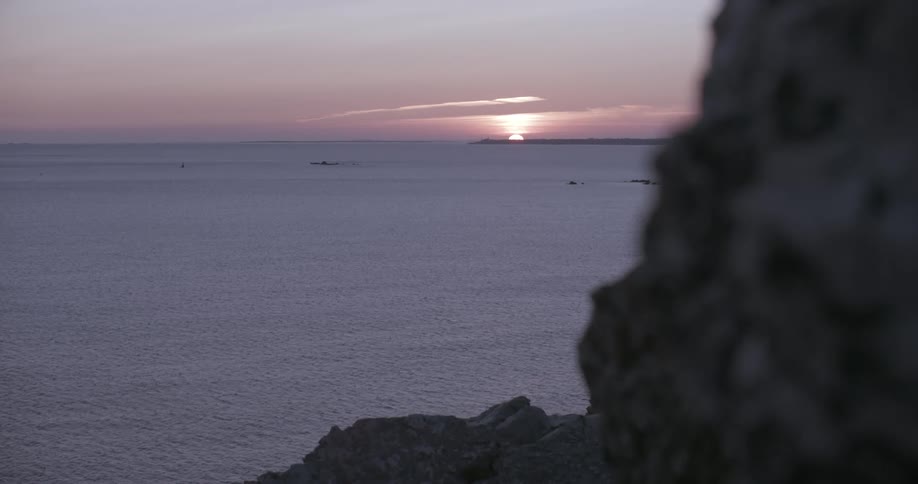 Beautiful landscape of the calm sea coast with the sun setting on the horizon in a purple sky