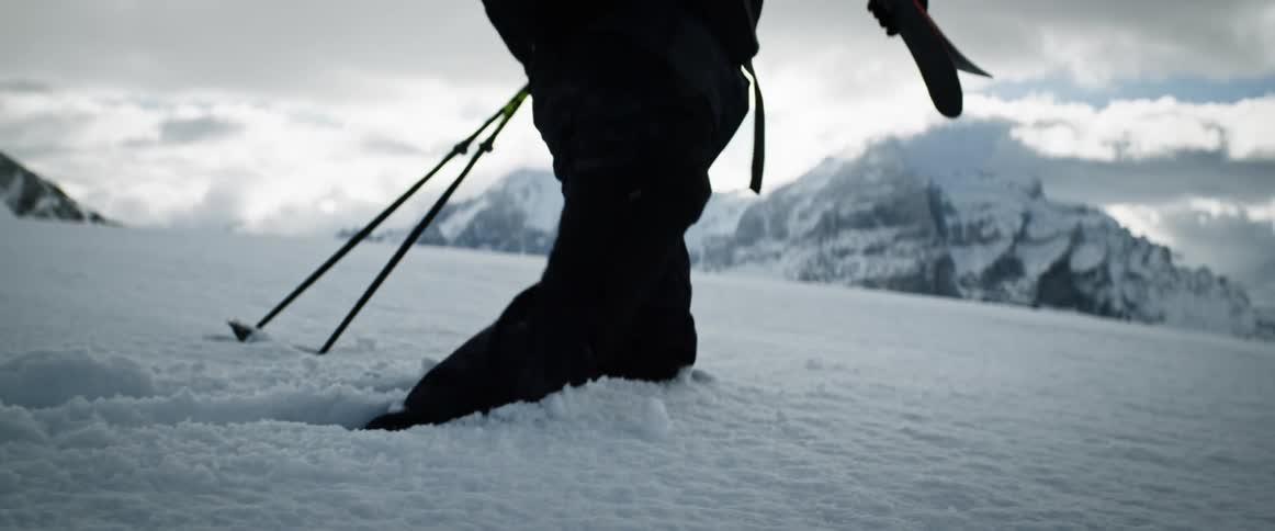 A couple of skiers is walking in the snow with mountains in the background