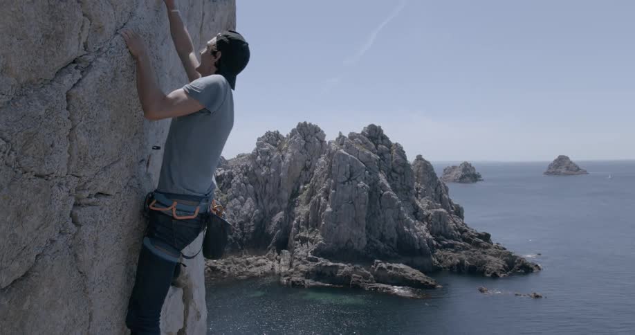 Man with seat belts climbing a mountain wall on a seaside cliff