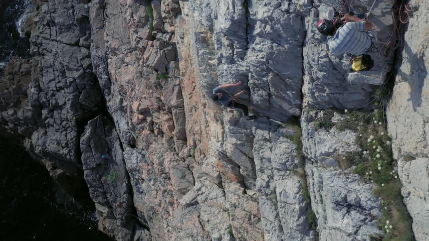 A man watches another man climb a cliff