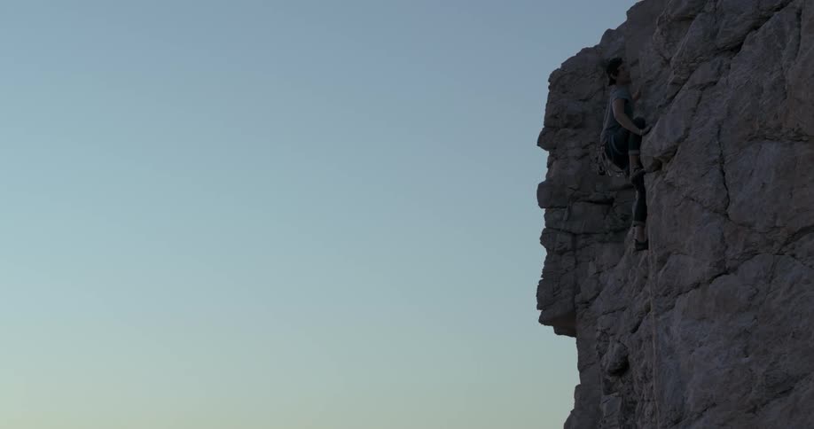 Man climbing the rocky wall of a mountain on a cliff in a morning