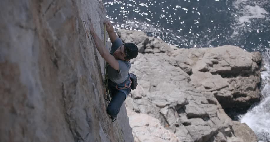 Man climbing a rock wall on the seaside coast and placing knives by a safety belt rope