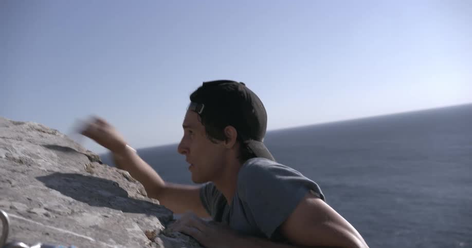 Man climbing a rocky wall of a precipitous mountain next to the sea