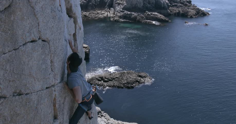 A male rock climbing on an island in the ocean