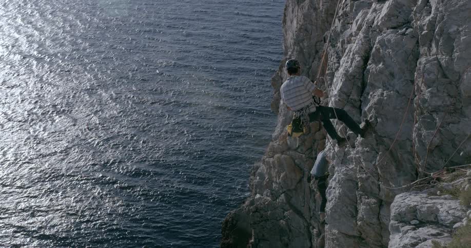 Two rock climbers climb a cliff over the ocean