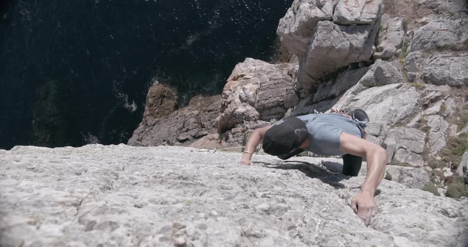 A person is rock climbing on a steep rugged cliff during next to the ocean