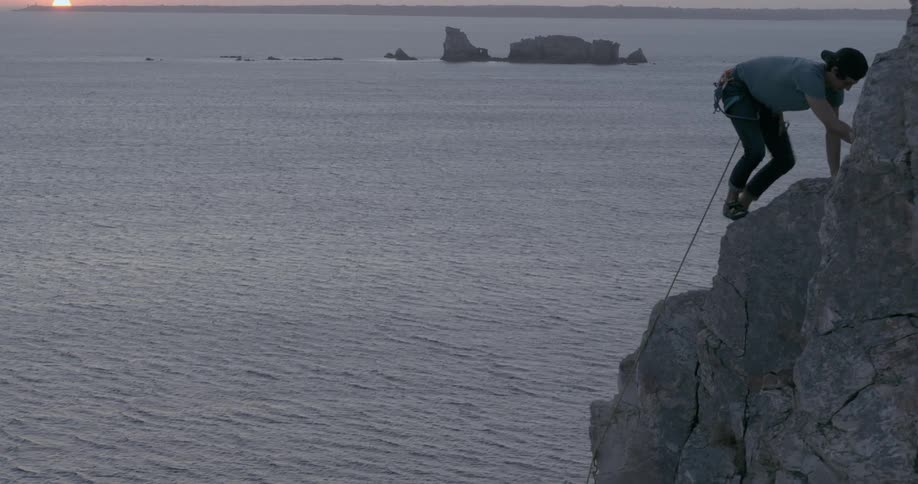 A person mountain climbing on a rock close to the ocean