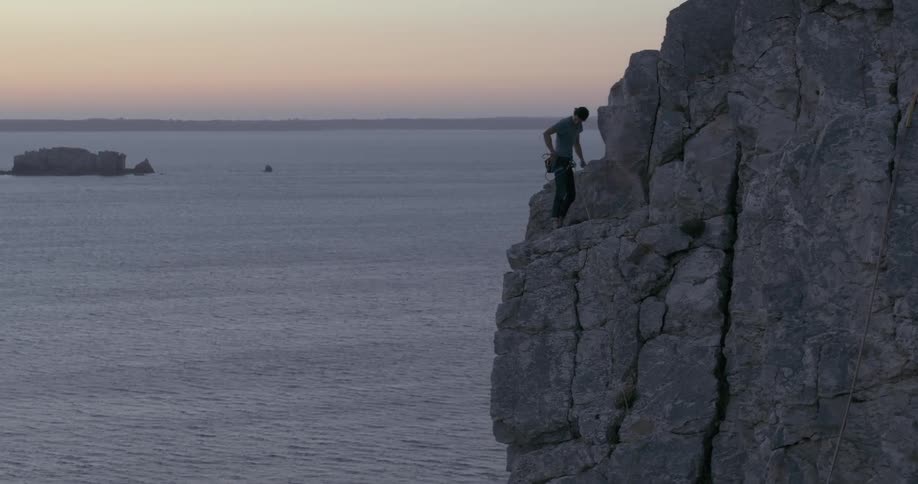 A rock climber prepares his rope to continue climbing a cliff over the ocean