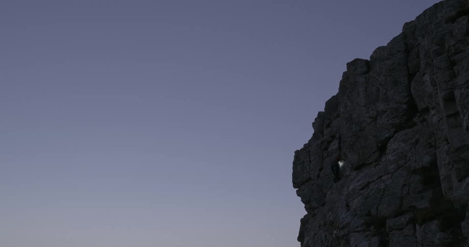 A person with a headlamp rock climbing on a cliff at dusk