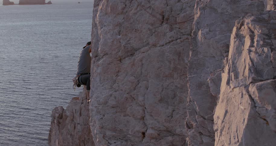 A climbers ascend a rugged cliff face next to the ocean