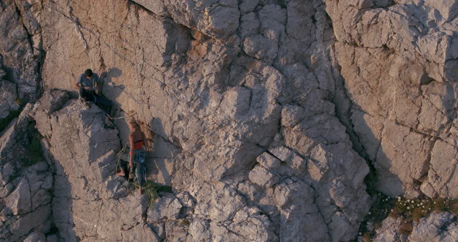 Two rock climbers tie knots on their ropes to continue climbing a cliff