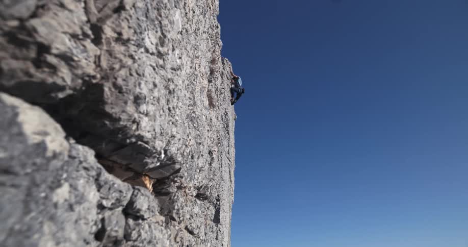 A man climbing a rock as he is almost at the top on a sunny day