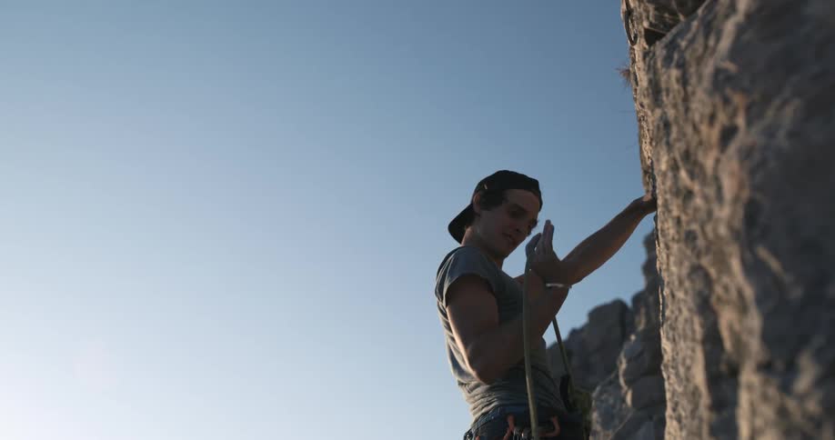 A climber is climbing a rocky surface against a clear sky using climbing equipment