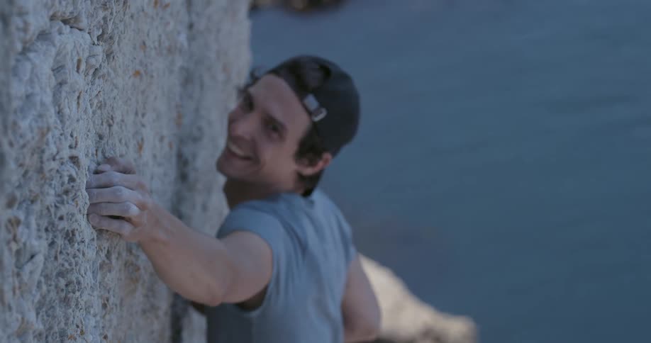 A man is climbing a rock near the sea during the day