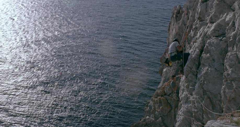 A man is hanging from a rope as he rock climbs