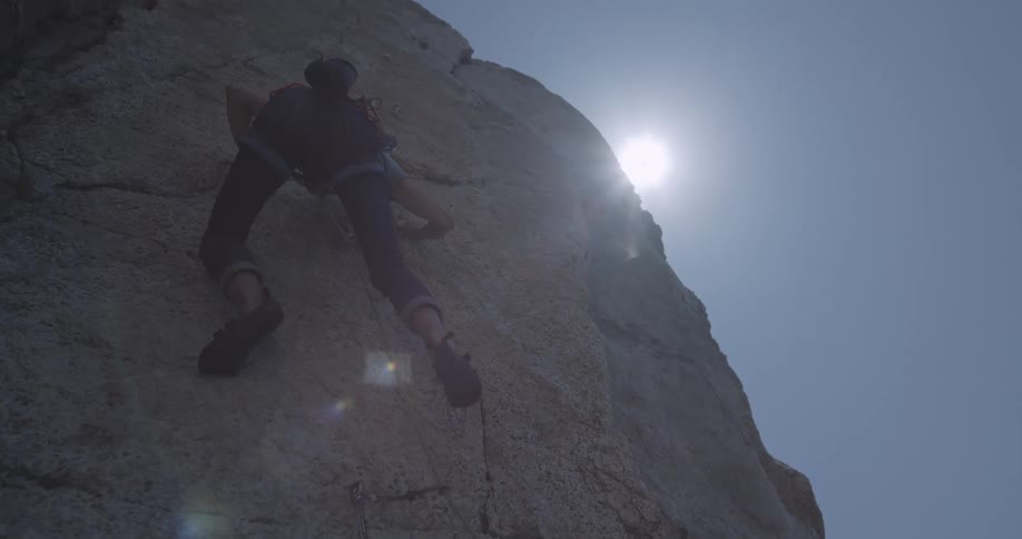 Man climbing a rocky wall of a mountain on a bright cloudless day