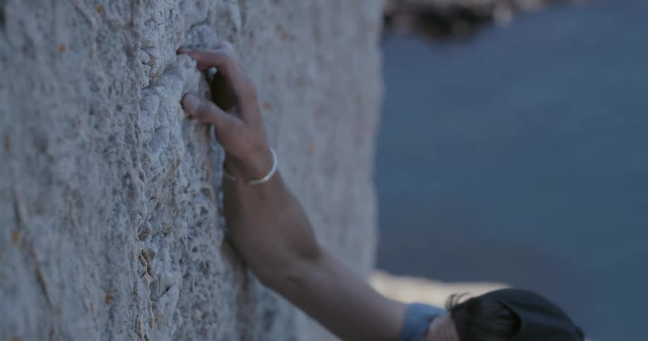 Man climbing a rock wall with abyss to the sea