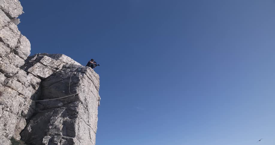 A bird flies past the man leaning over the cliff